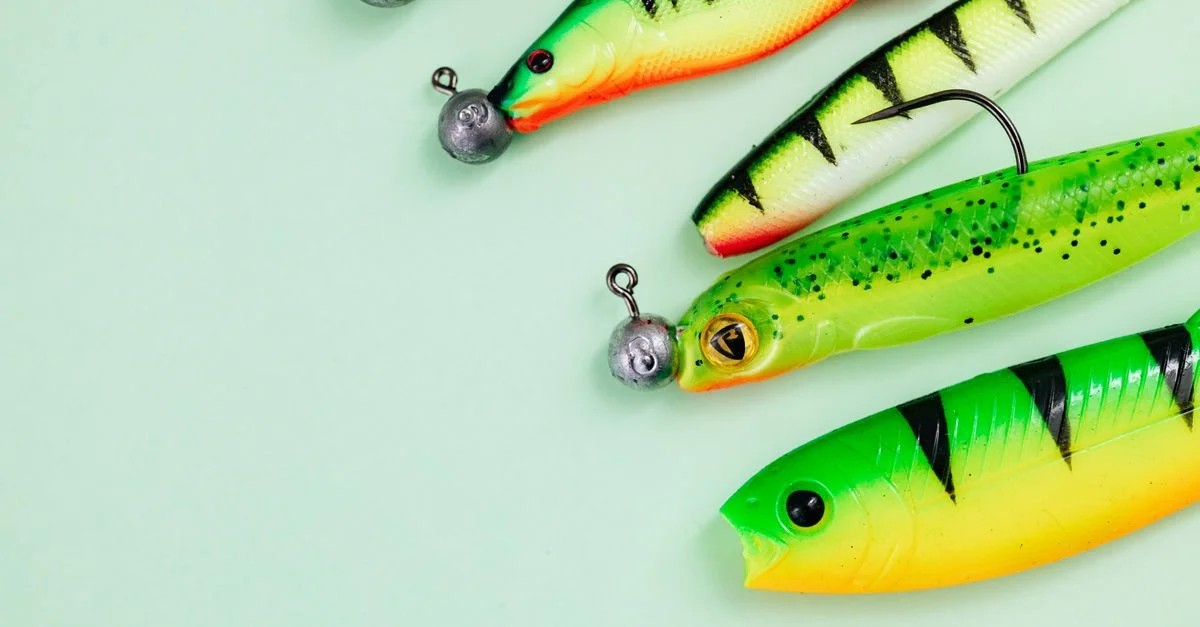 Assortiment vibrant d'appâts de pêche avec hameçons et poids sur une surface verte pastel.