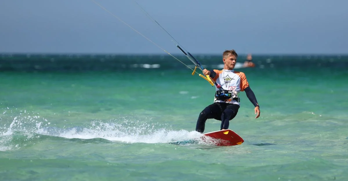Un homme profitant du kitesurf sur un océan bleu clair sous un ciel ensoleillé. Activité aquatique parfaite pour les amateurs de sensations fortes.