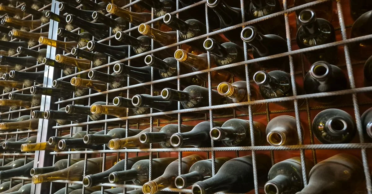 Des rangées de bouteilles de vin vides stockées horizontalement dans un casier métallique.