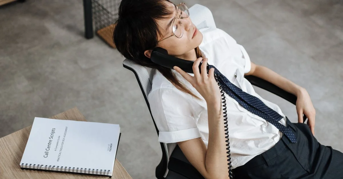 Un jeune professionnel agent de centre d'appel se détendant dans un fauteuil de bureau tout en tenant un téléphone, suggérant un environnement de travail décontracté.
