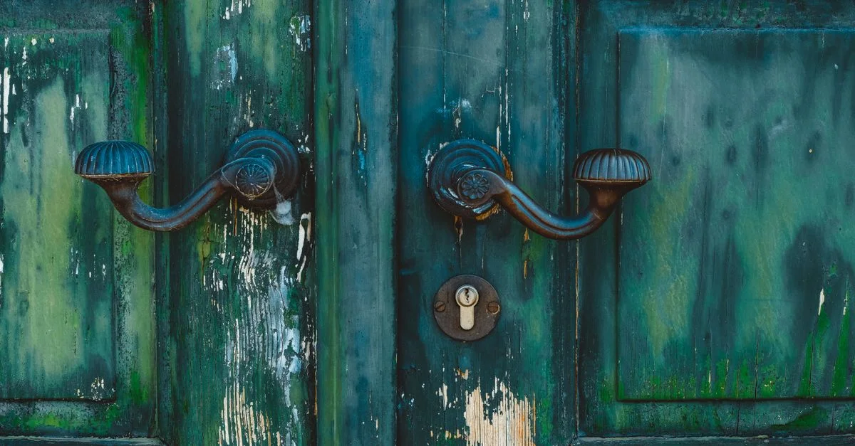 Gros plan sur une porte en bois vintage avec des poignées en fer et un trou de serrure, présentant de la peinture verte écaillée.