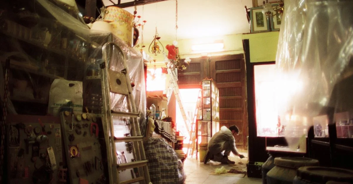 Un artisan travaillant dans un atelier encombré rempli d'échelles et d'objets faits à la main.