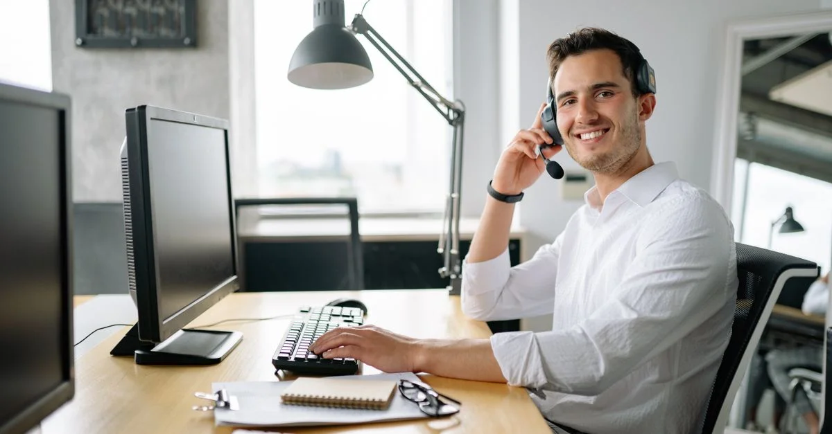 Agent de centre d'appels souriant travaillant à un bureau avec un casque et un ordinateur dans un bureau moderne.