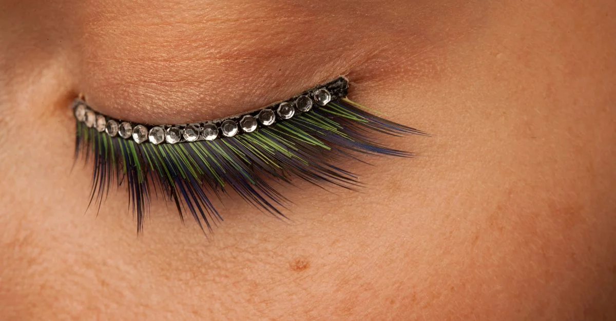 Un gros plan frappant de cils avec des plumes colorées et des strass, mettant en valeur un maquillage artistique de mode détaillé.