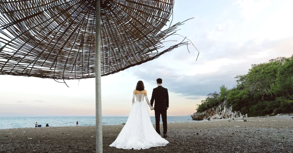 Les mariés se tiennent la main sur une plage sereine d'Antalya au coucher du soleil, sous un parasol.