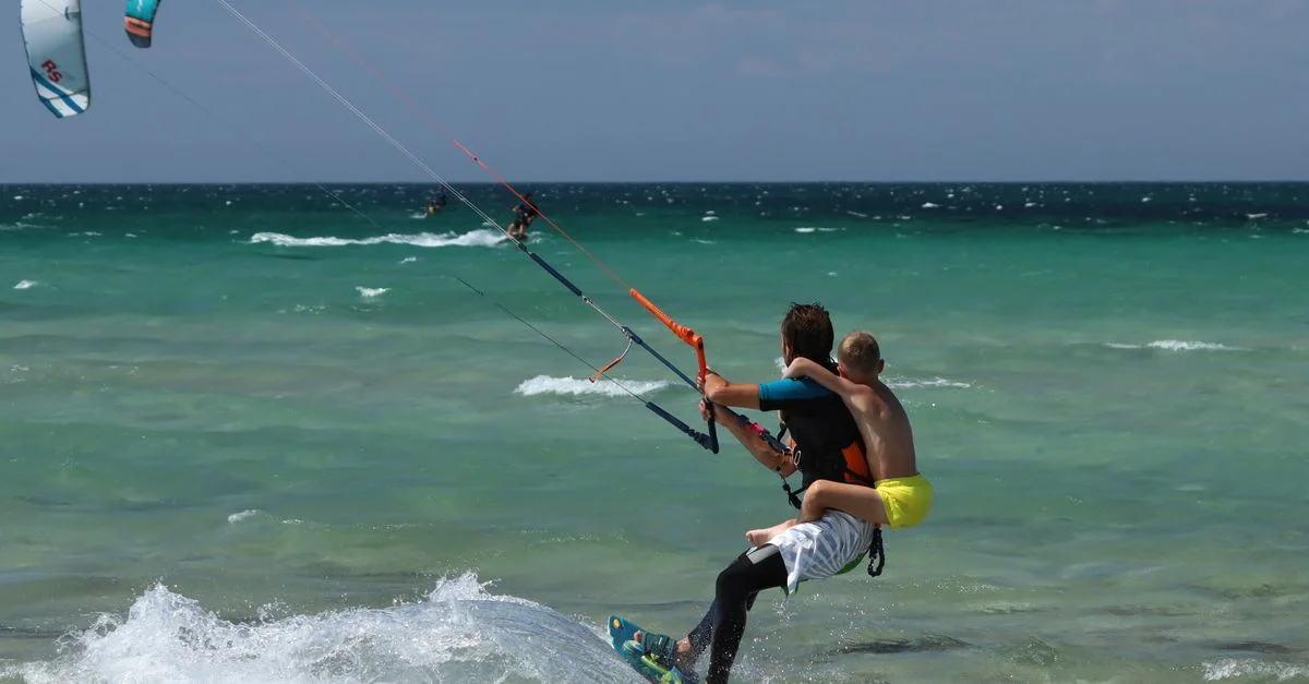 Scène dynamique d'un père et de son fils faisant du kitesurf ensemble par une journée ensoleillée à la plage.