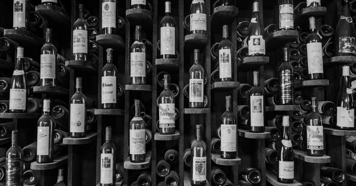 Une photo en noir et blanc mettant en valeur un élégant présentoir à vin rempli de différentes bouteilles.