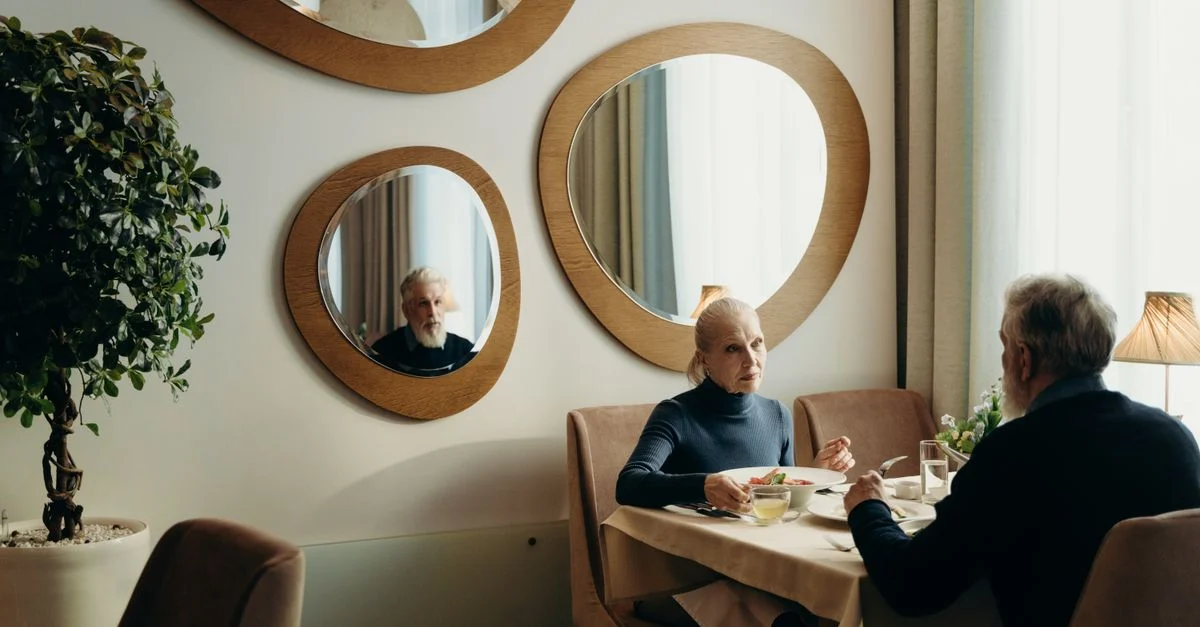 Un couple âgé déguste un repas dans un restaurant confortable avec un éclairage chaleureux et une décoration élégante.