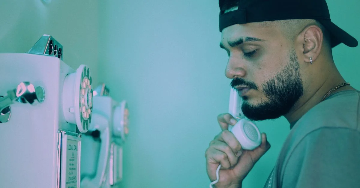 Un homme barbu portant une casquette utilisant un téléphone vintage avec un éclairage d'ambiance teal.