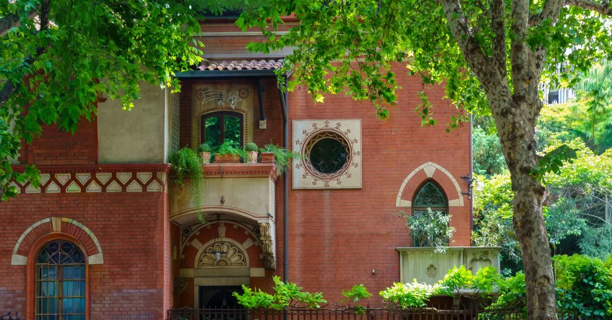 Une magnifique villa en briques rouges entourée d'une végétation luxuriante et ornée de détails architecturaux.