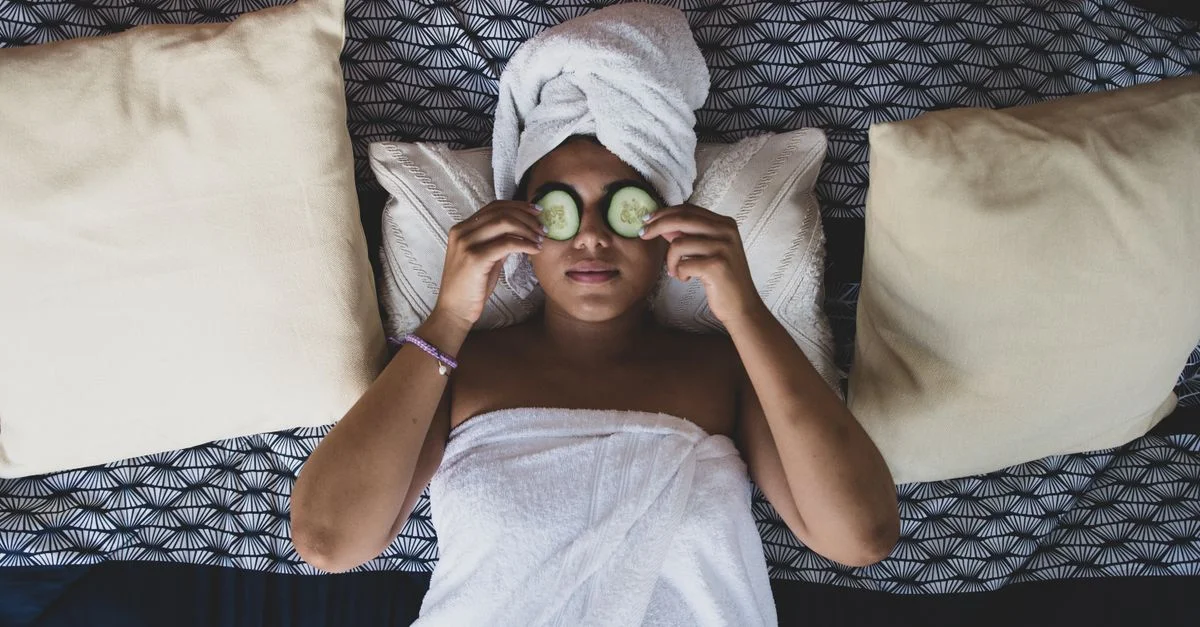 Femme profitant d'un rituel de soins de la peau relaxant avec des concombres sur le lit, enveloppée dans une serviette.