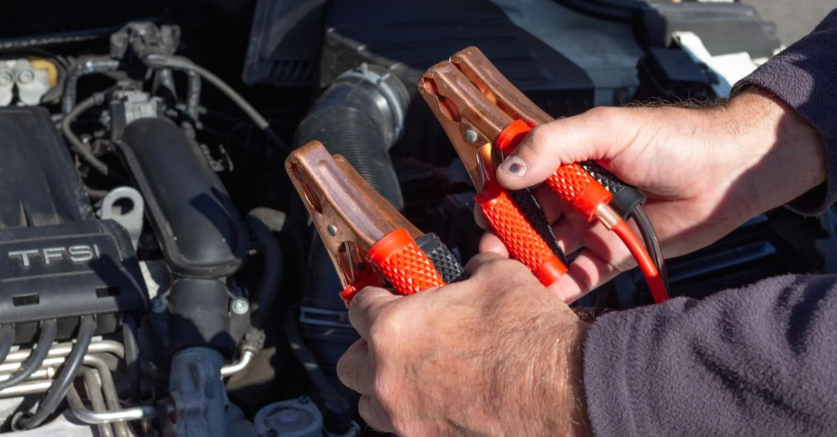 Gros plan sur des mains tenant des câbles de démarrage près d'un moteur de voiture, prêtes pour la réparation.