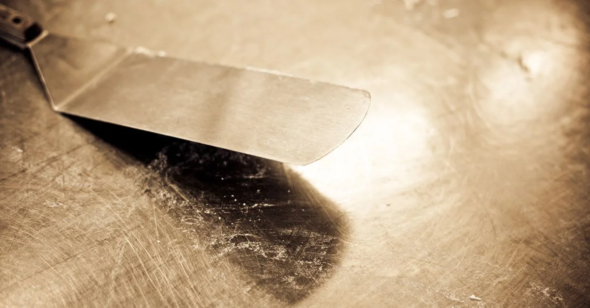 Gros plan d'une spatule en acier inoxydable vintage sur un plan de travail usé avec des tons sépia.