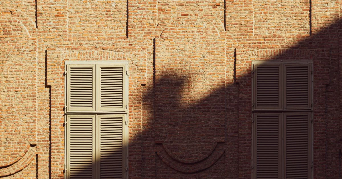 À Turin, en Italie, la douce lumière du soleil projette des ombres sur un mur de briques aux volets en bois fermés.