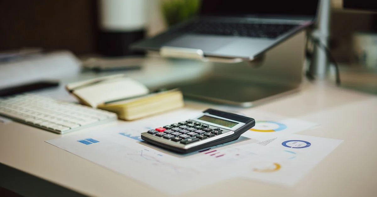 Un espace de travail moderne avec un ordinateur portable, une calculatrice et des documents sur un bureau, parfait pour des tâches financières.