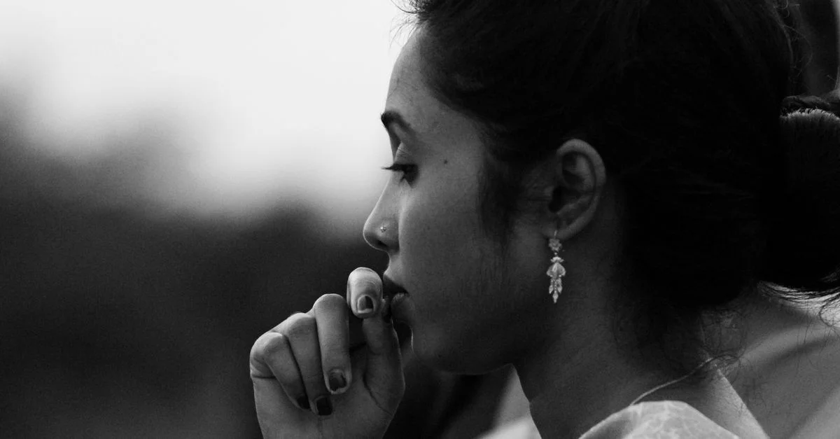 Profil latéral d'une femme en niveaux de gris, reflétant une profonde réflexion, mettant en valeur son bijou d'oreille.