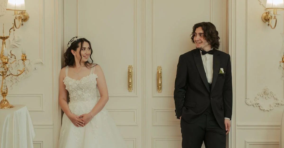 Un couple de mariés souriant l'un à l'autre à l'intérieur, capturant un moment de mariage romantique avec un décor élégant.