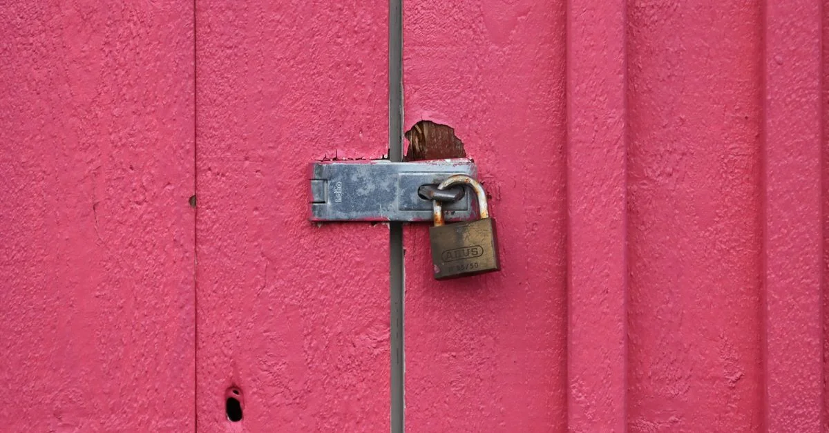 Gros plan d'un cadenas rouillé sécurisant une porte en métal rose vif, montrant des signes d'usure.
