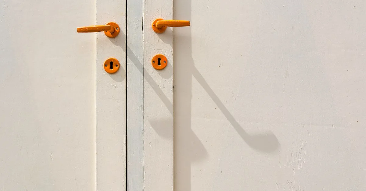 Gros plan minimaliste sur une porte blanche avec des poignées orange et des ombres, créant une esthétique moderne.